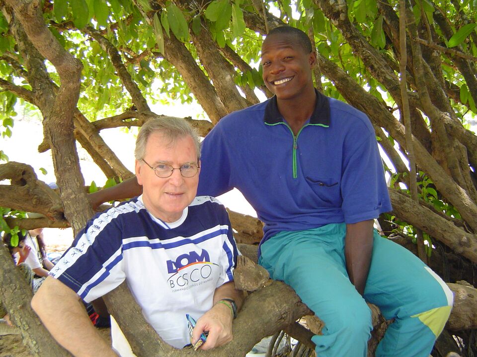 Siegfried Zilz sentado num galho de árvore ao lado de um amigo africano, ambos sorrindo