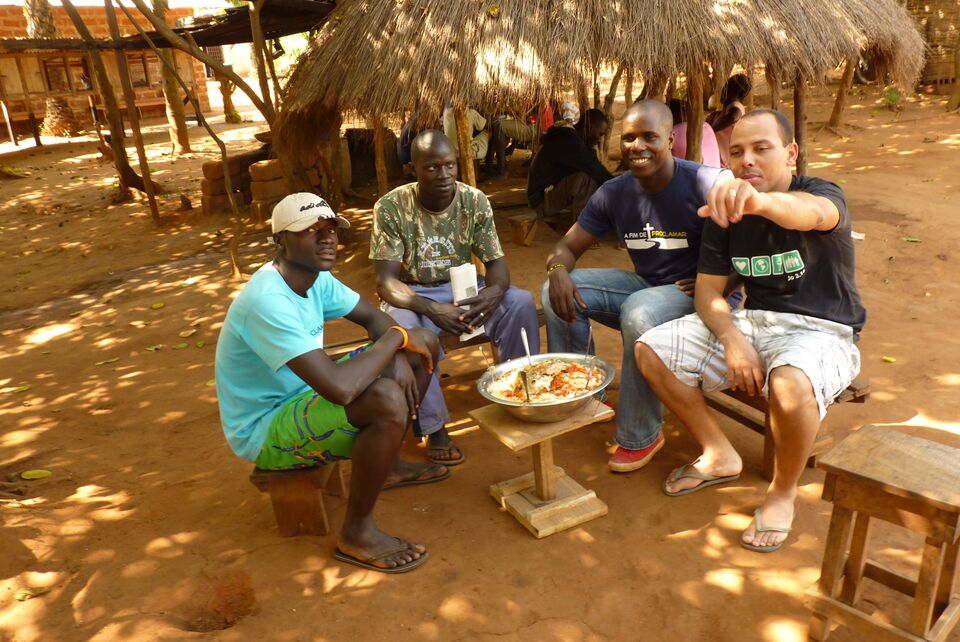 Voluntários e irmãos guineenses à mesa sob um telhado de palha