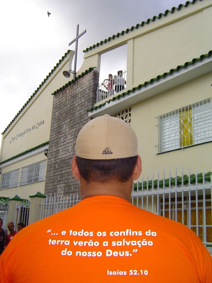 Jovem de camiseta laranja com versículo de Isaías, diante de uma igreja