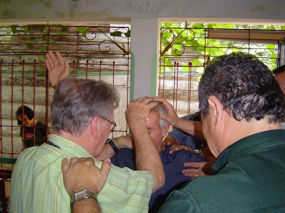 Irmãos orando com as mãos sobre um homem