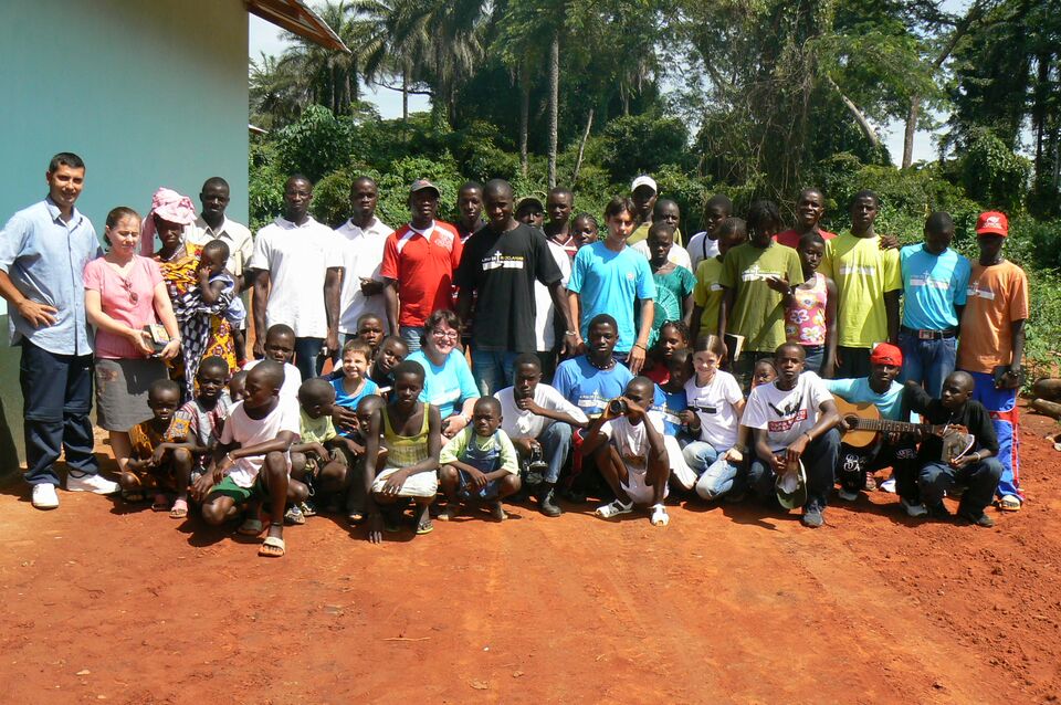 Grande grupo de irmãos guineenses e brasileiros reunidos numa estrada de terra vermelha